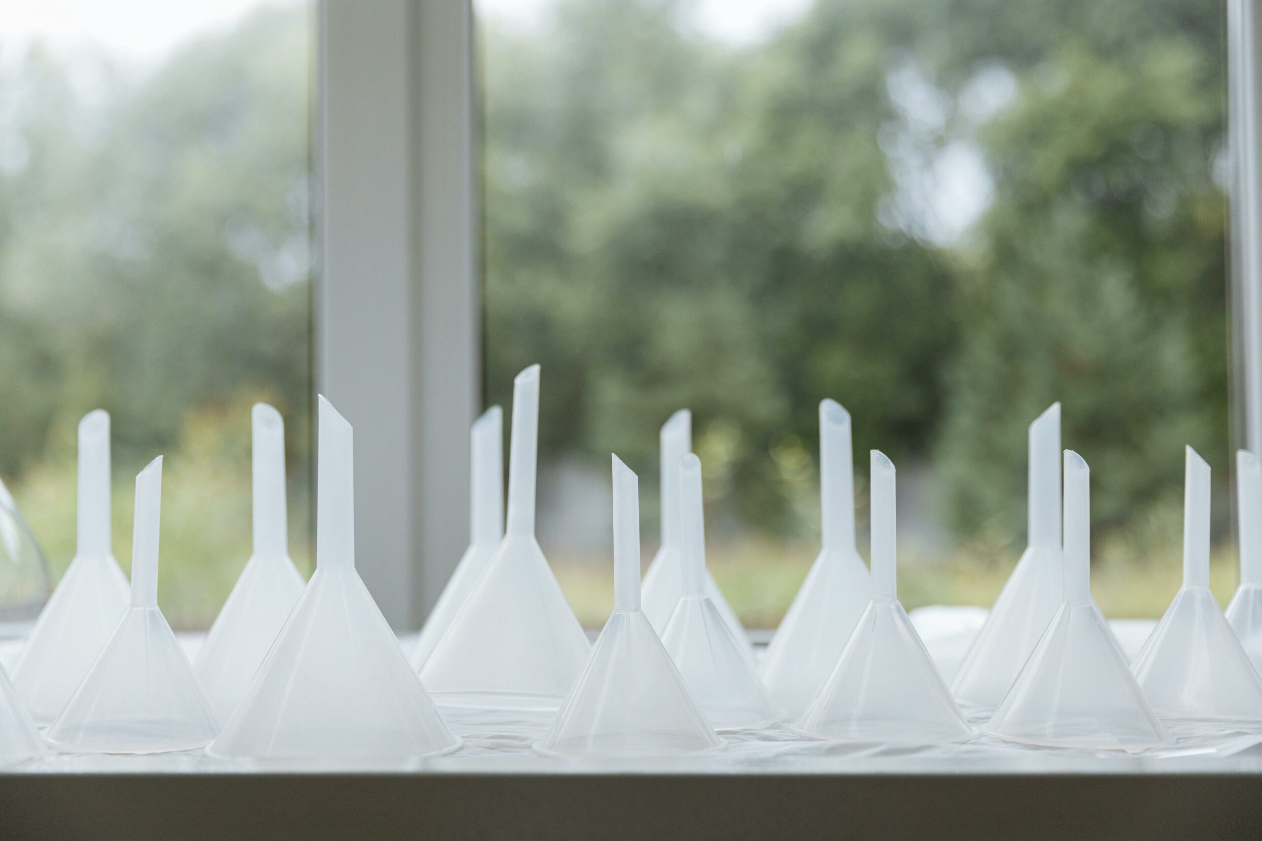 White plastic funnels arranged near a window with greenery outside.
